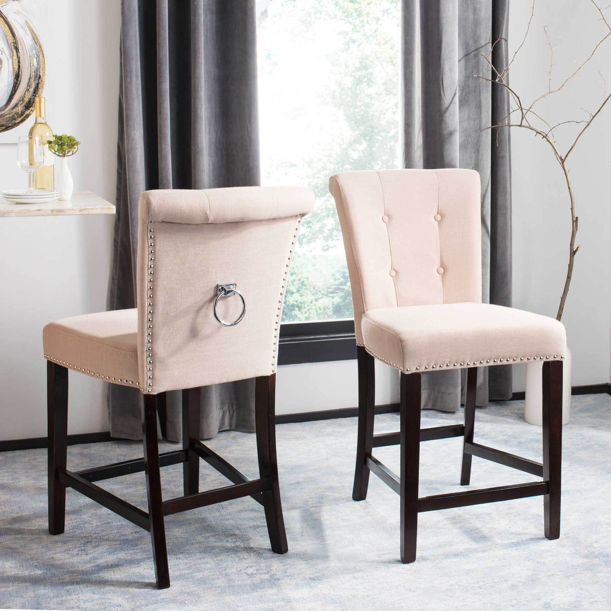 Two beige linen counter stools combine tufted backrests, a chrome back ring, and espresso wood footrests.