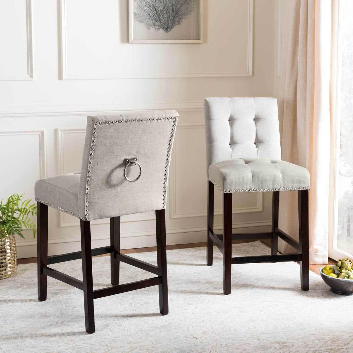 Matching light gray counter stools display tufted seats and metal ring details above dark wood legs