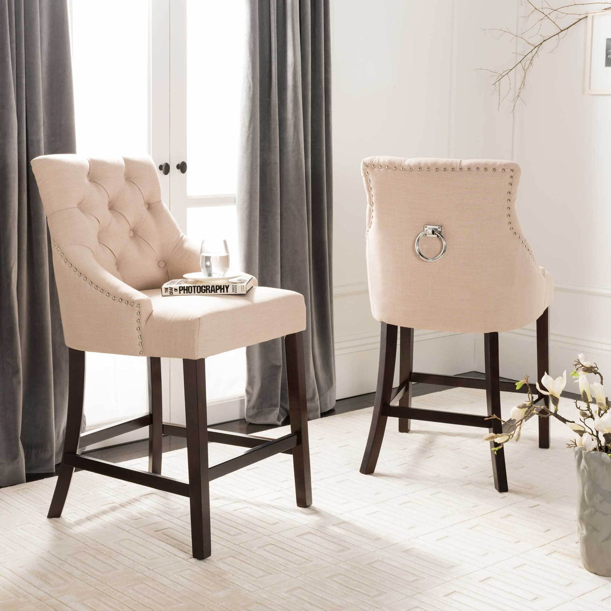Tufted beige linen counter stools bring curved comfort, chrome rings, and dark wood legs to a bright room.