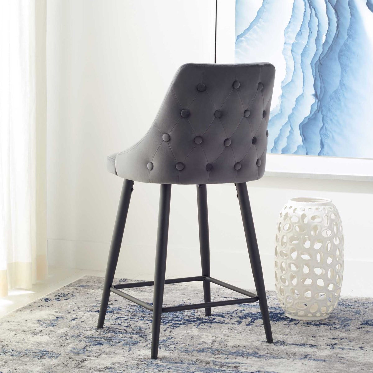 Fabric-covered buttons accent the curved velvet back of this counter stool with slender black metal legs
