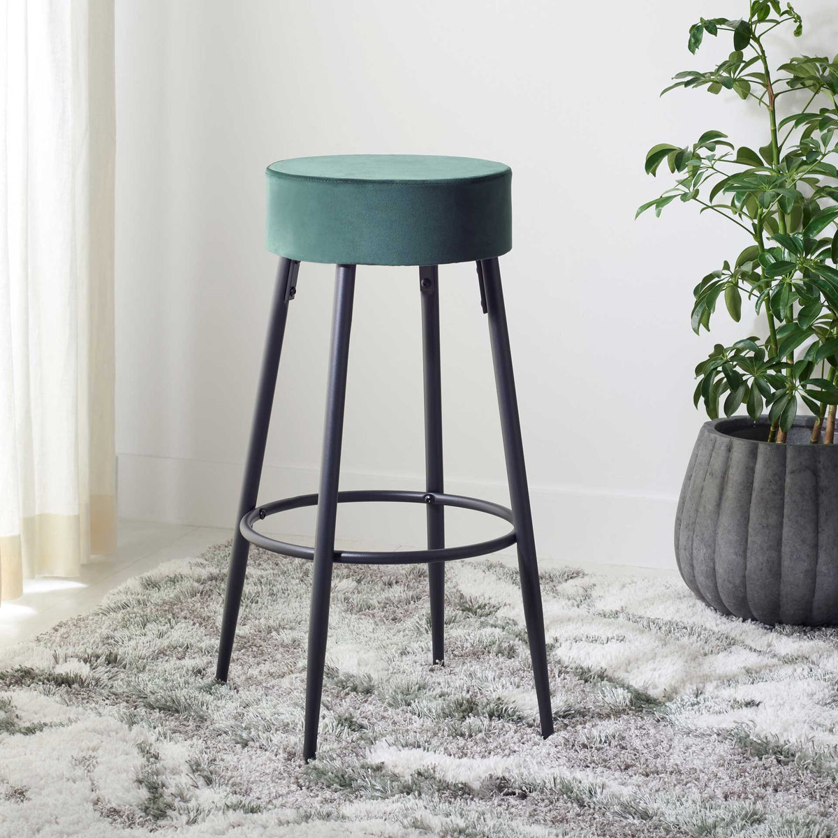 A rich green velvet seat adds a bold touch to this airy black metal counter stool