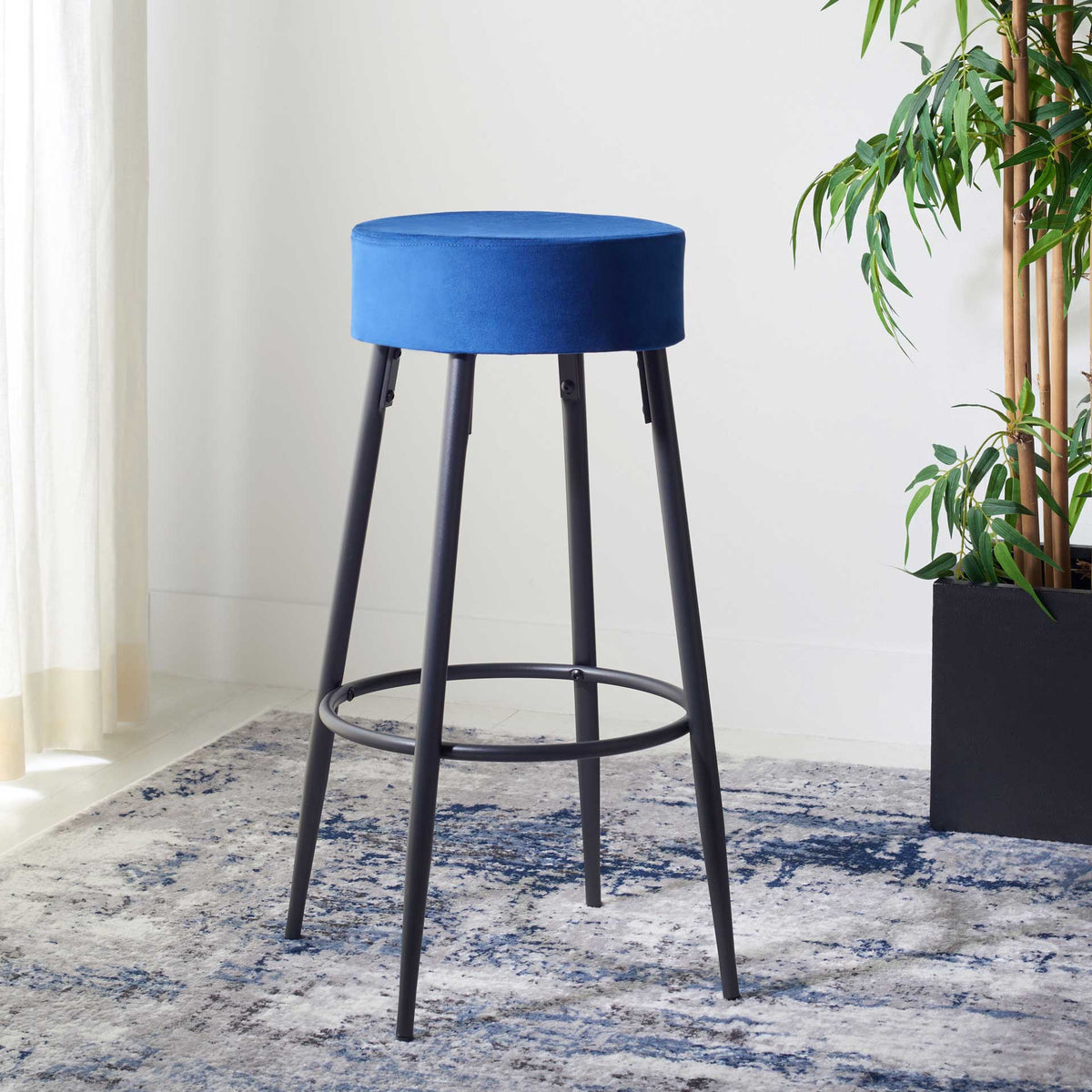 A blue velvet seat and slender black frame lend this round stool modern style