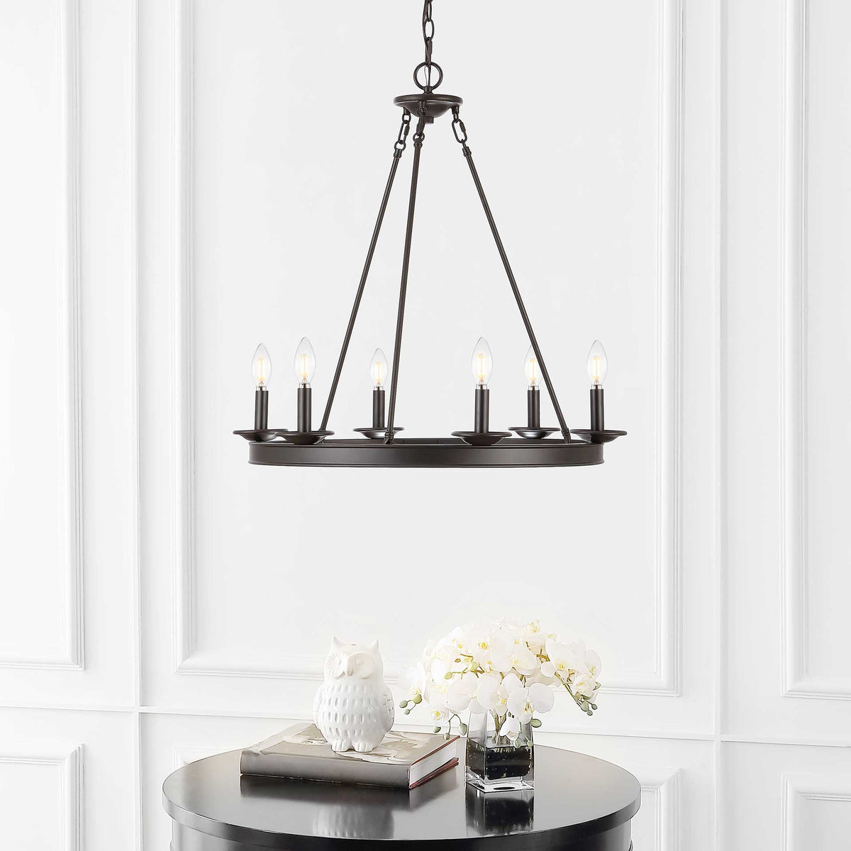 Six softly glowing candle-style bulbs warm a bronze ring chandelier above a black table.