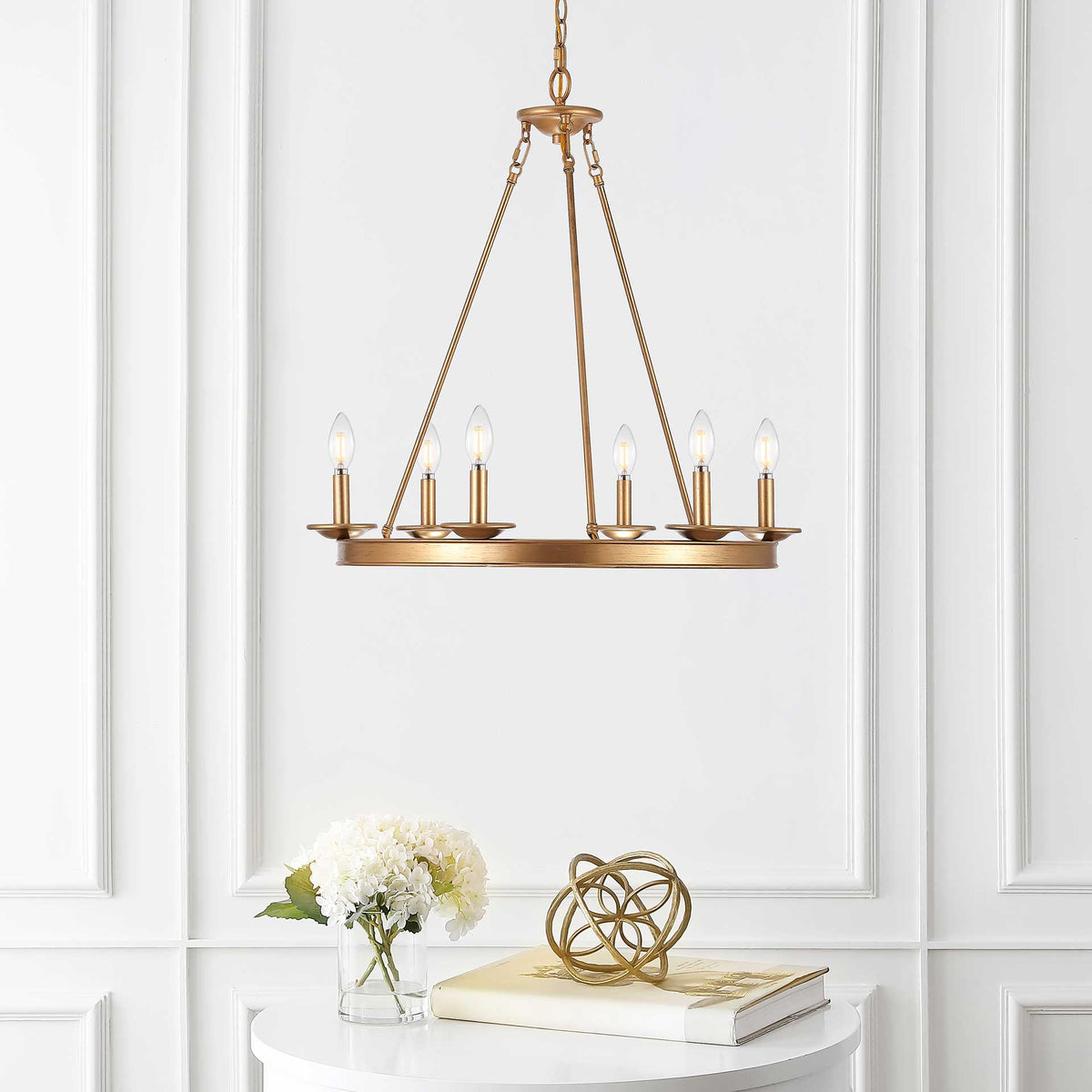 Six glowing candle-style bulbs warm a gold ring chandelier above a white table.