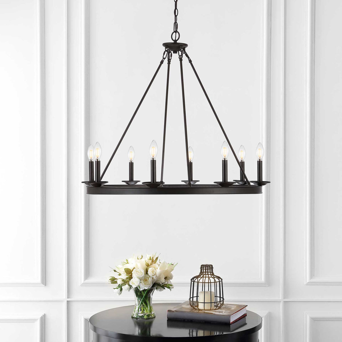 Eight glowing bulbs illuminate a bronze chandelier above a black table and white flowers