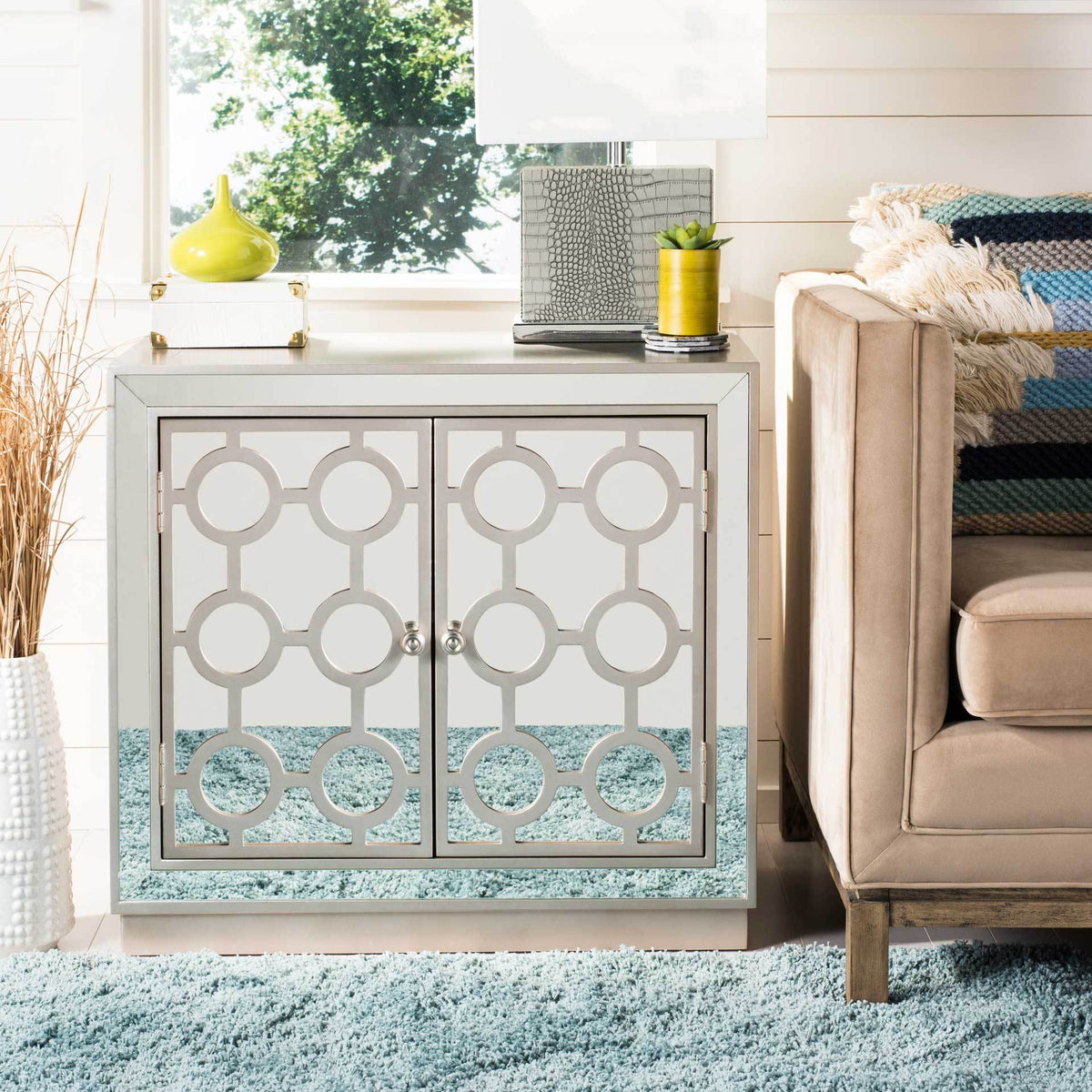 A champagne chest shines with mirrored doors and a repeating circular design beside a sofa