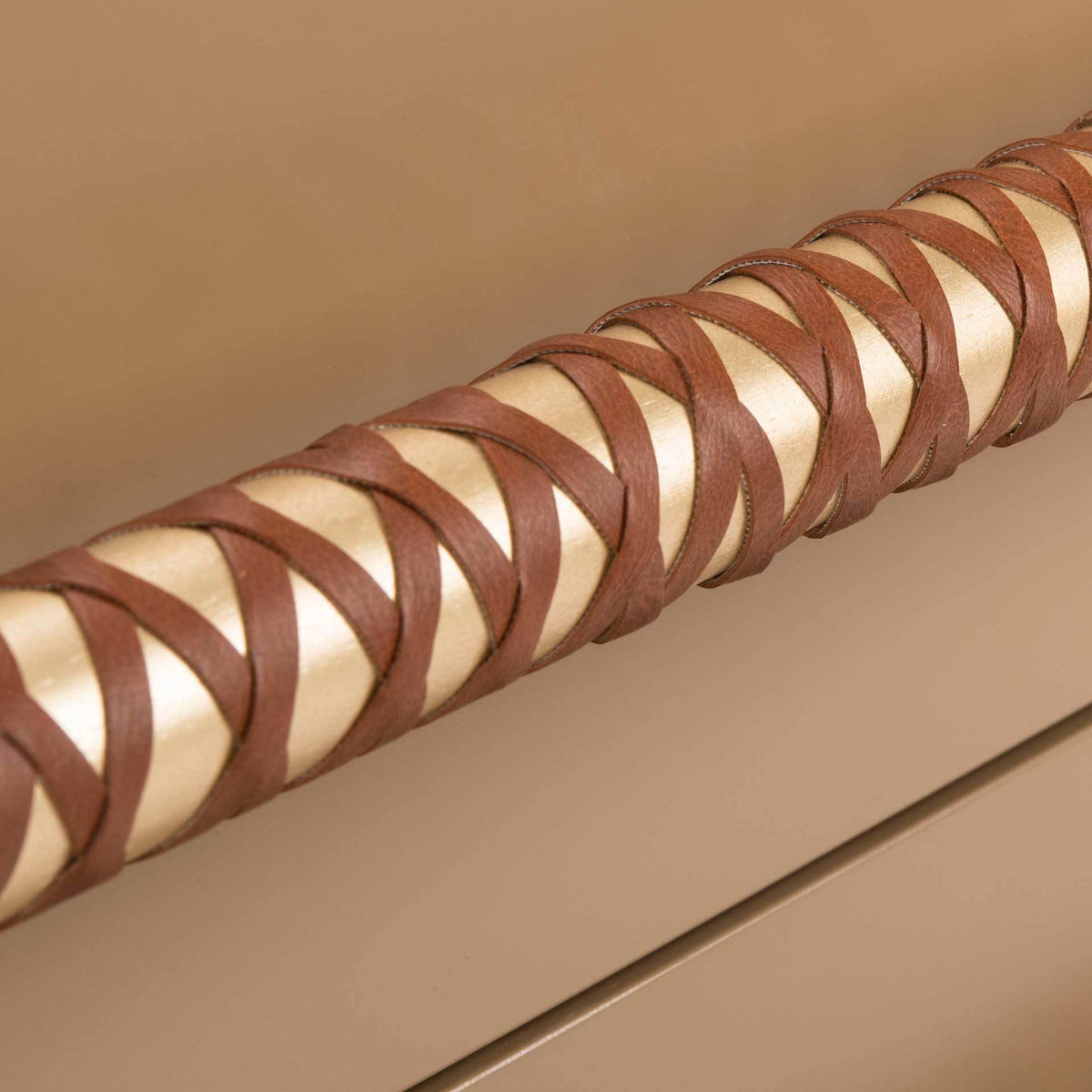 Brown faux leather lacing winds around a gold pull for warm texture against the taupe drawer