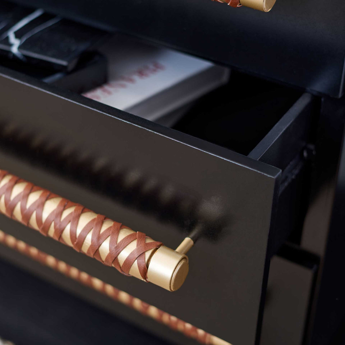 An open black drawer offers accessible storage beneath a gold pull wrapped in brown faux leather