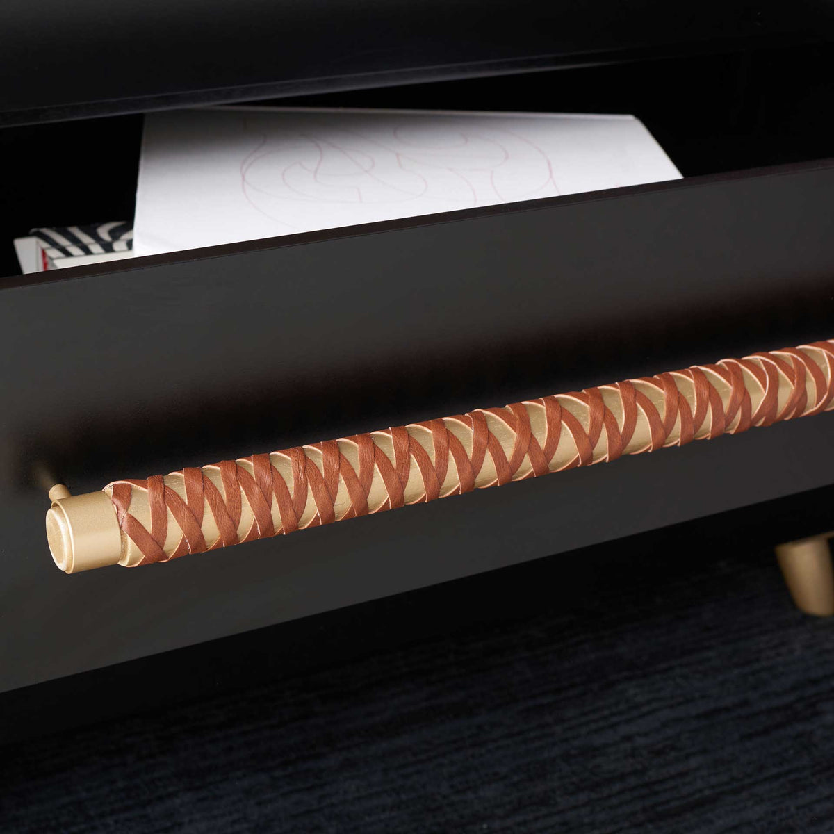 A long gold pull wrapped in brown faux leather adds texture to the smooth black drawer front