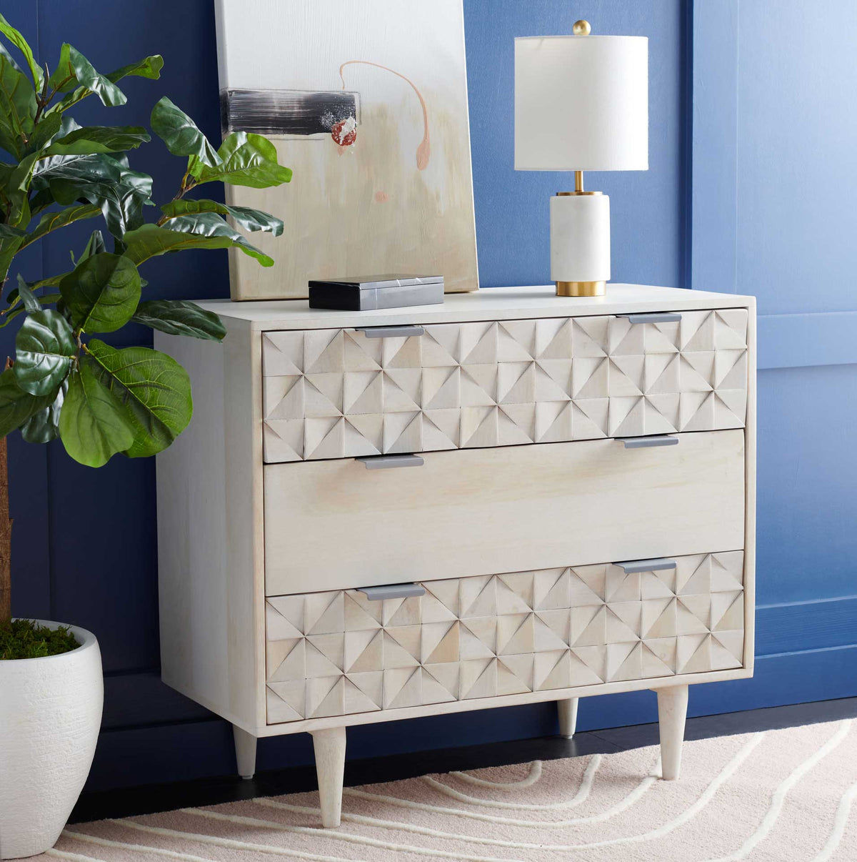 Silver pulls glint against sculpted whitewashed drawers in a colorful living space.
