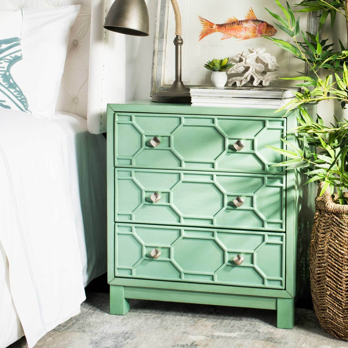 Turquoise three-drawer chest adds sculpted storage and silver-tone accents beside a bed.