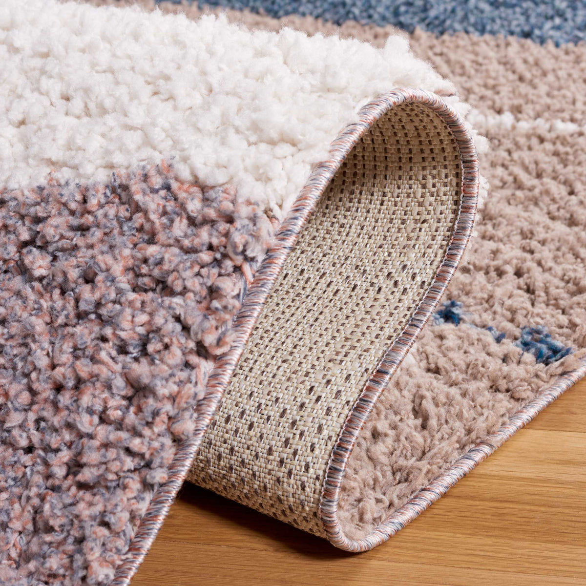 A rolled rug edge reveals woven backing beneath fluffy blue and ivory pile