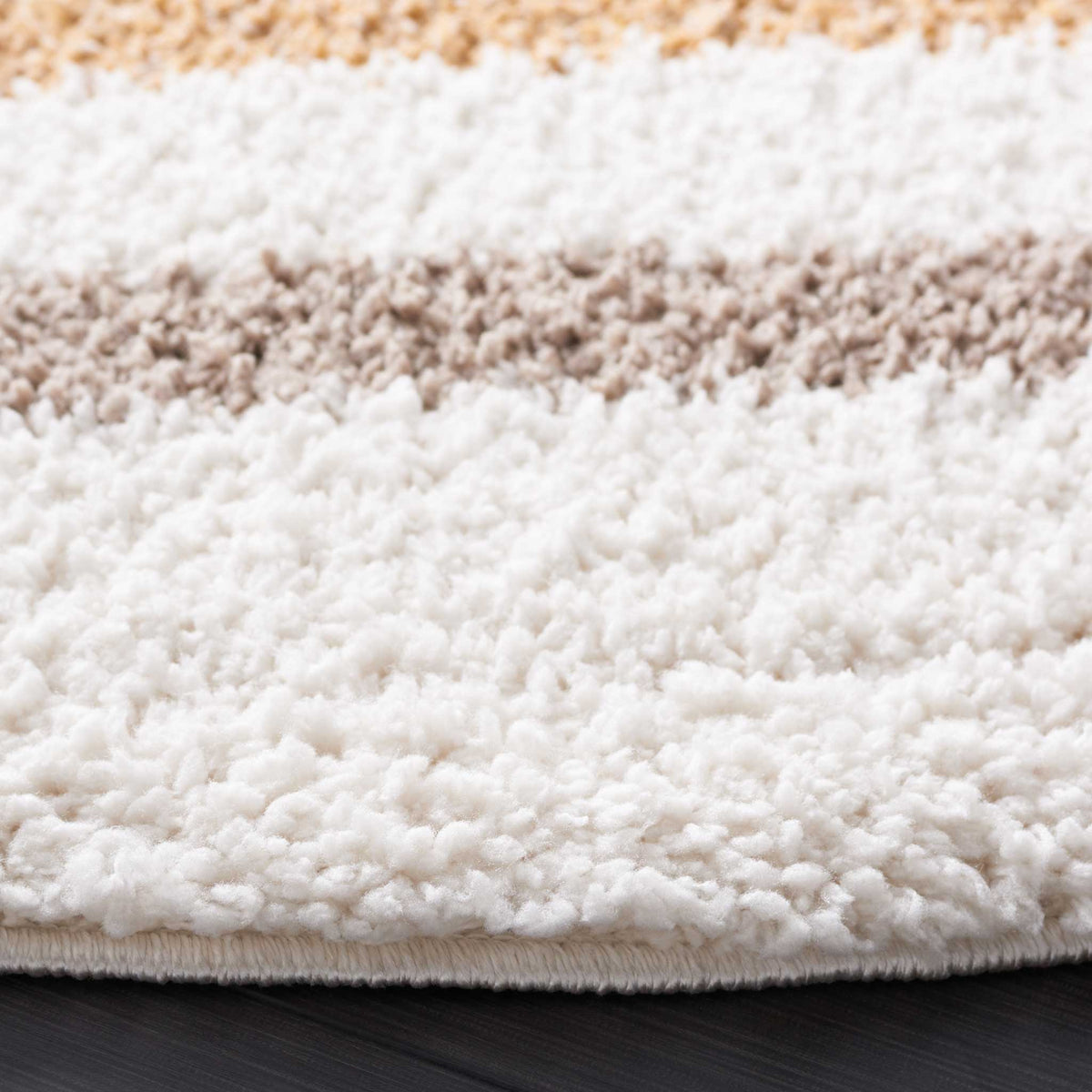 Dense ivory shag is accented by soft taupe and warm gold near a finished edge