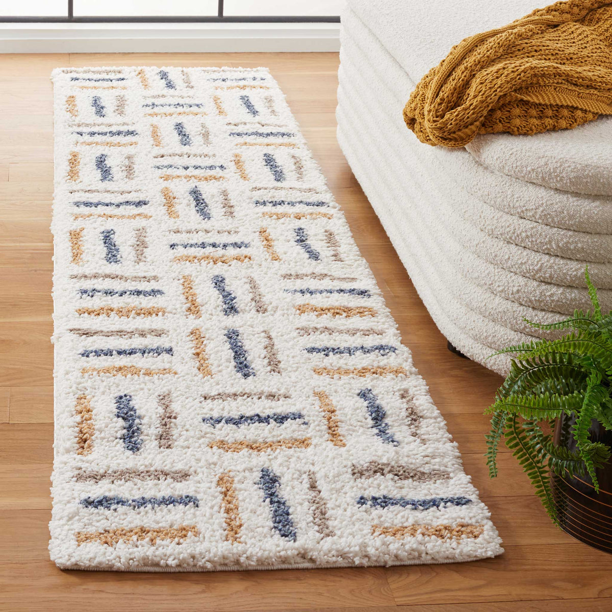 Raised blue, gold, and taupe dashes create a textured grid across the plush ivory runner.