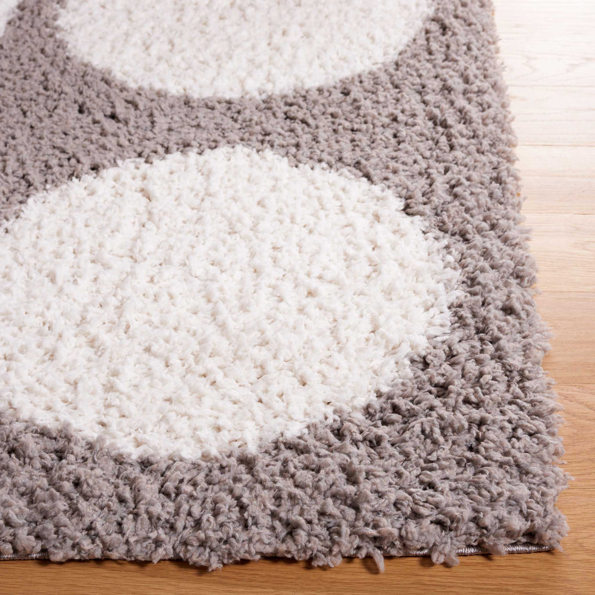 Rounded ivory motifs pop against plush gray fibers at the rug's edge