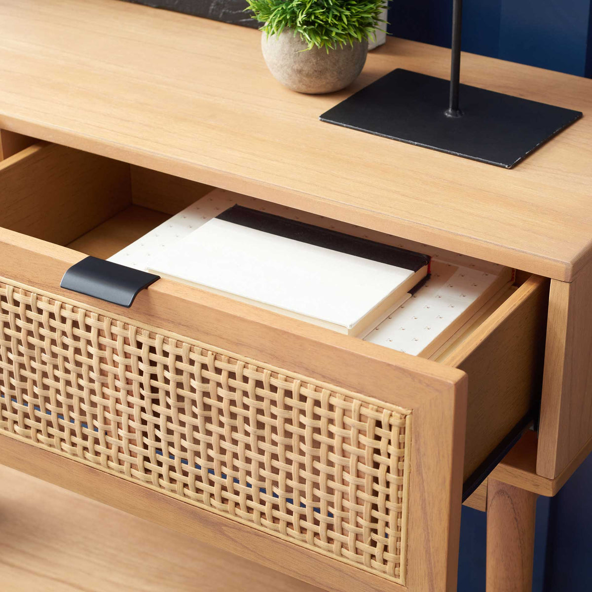An open rattan-front drawer holds papers beneath the smooth natural wood top.