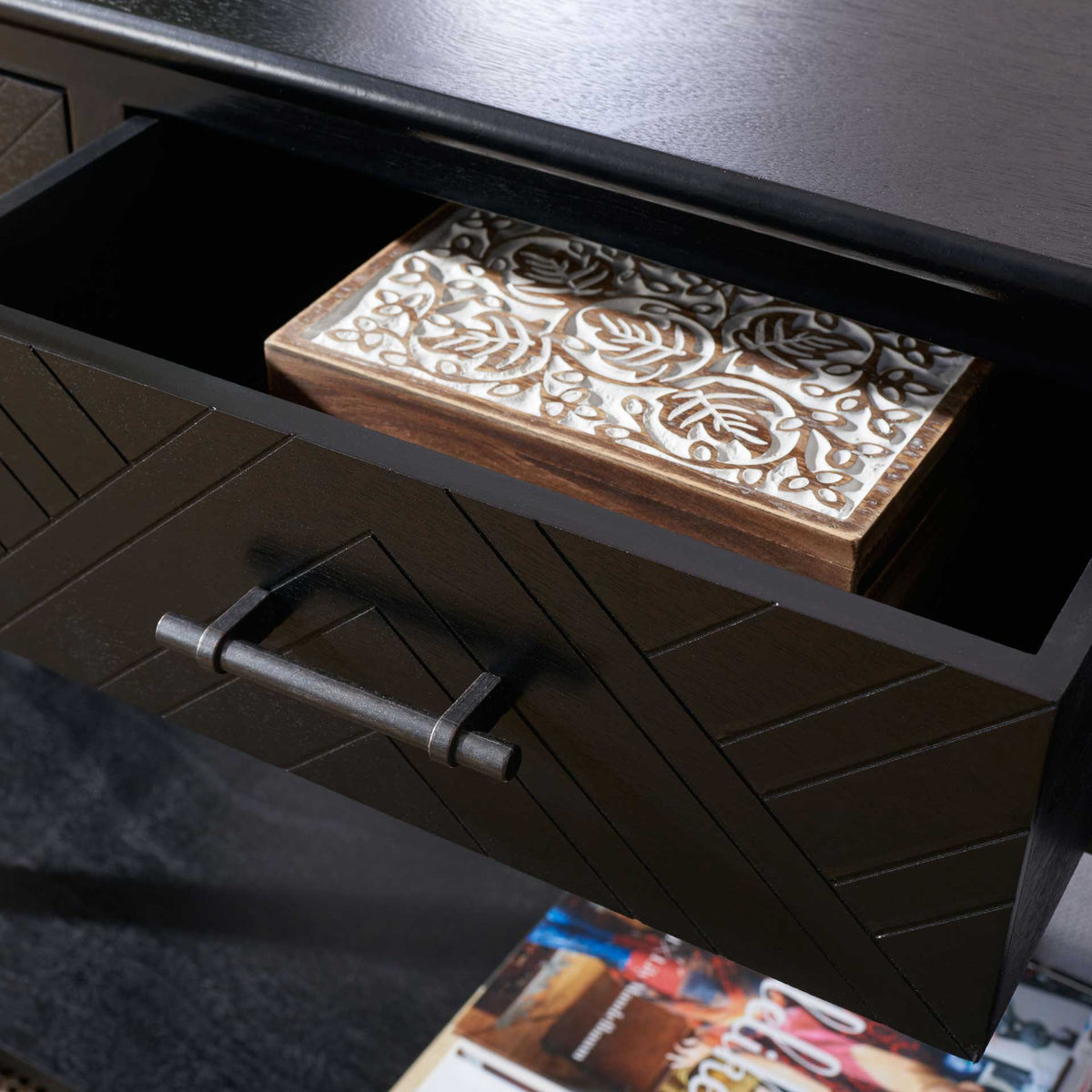 An open drawer keeps decorative treasures tucked away beneath the black console's wood-grain top