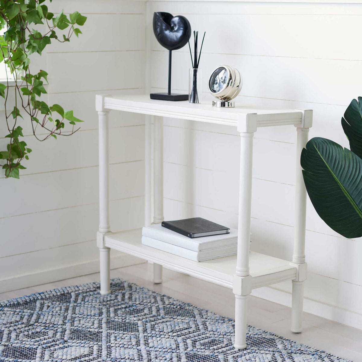 A bright white console offers an open lower shelf for books beneath its decorated top.