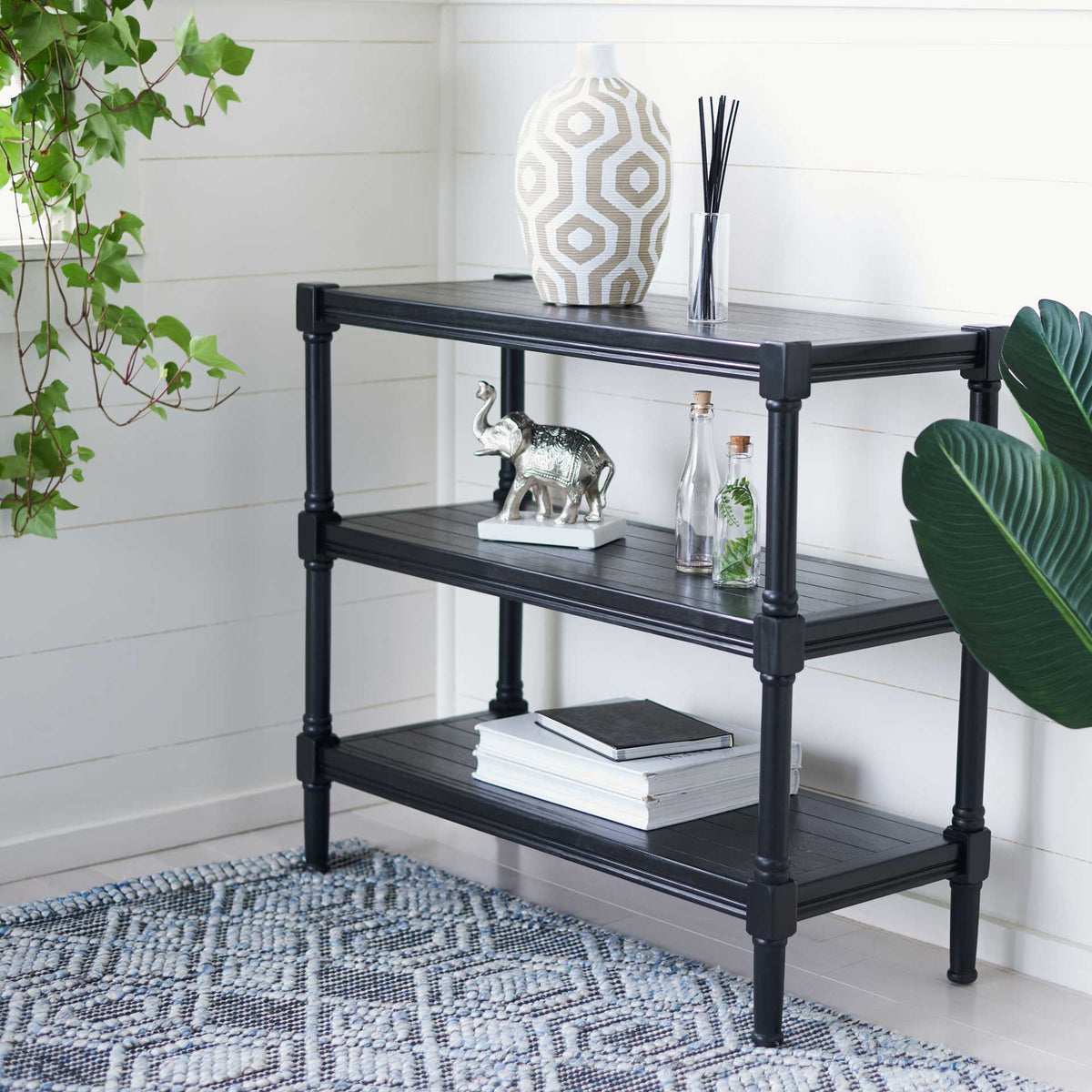 The black three-tier console holds books and decorative accents against white paneled walls.