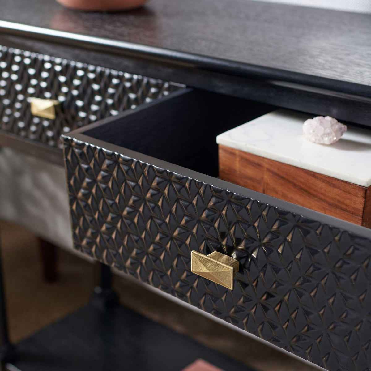 An open drawer tucks away small essentials behind a patterned black front and bronze-tone pull.