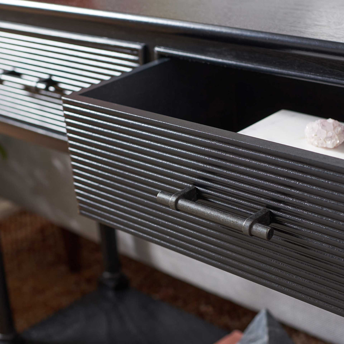 The open drawer reveals storage behind its ribbed black front and metal pull.