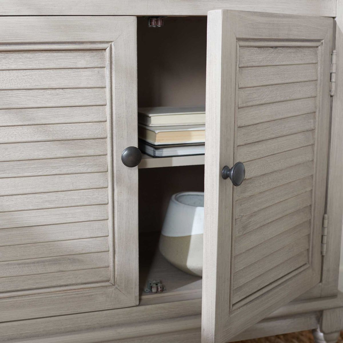 An open louvered cabinet door reveals a shelf for books and decorative accents.