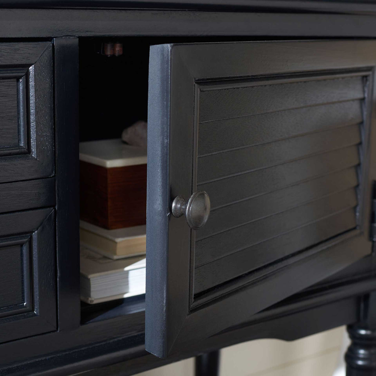 An open black slatted door reveals a cabinet nook for stacked books and small essentials.