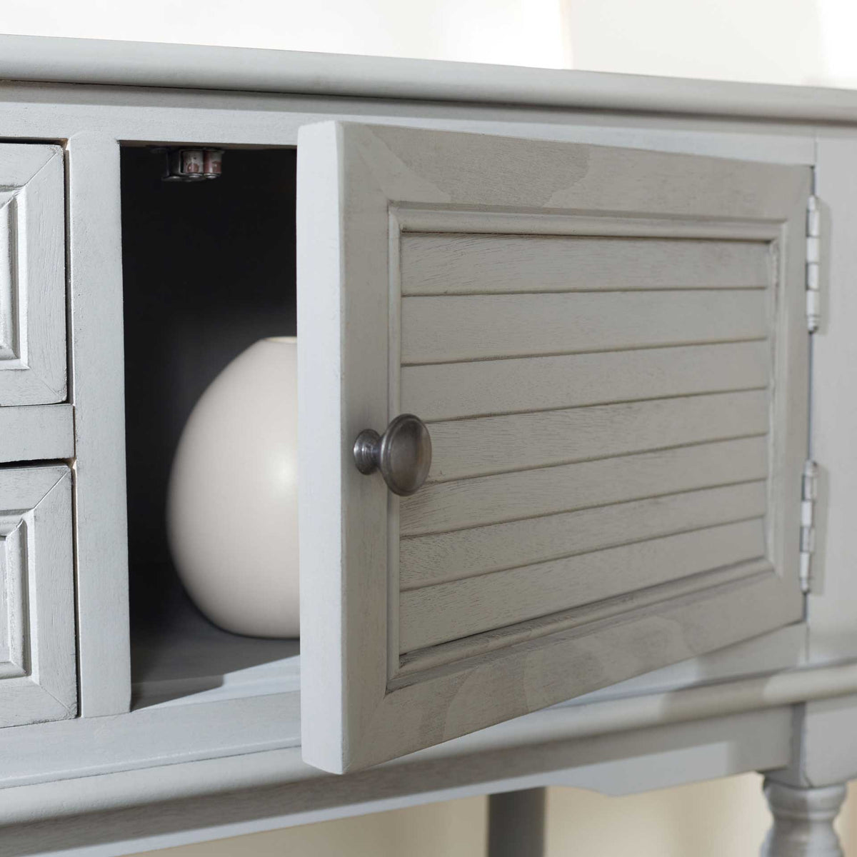 An open slatted door reveals a roomy compartment behind the distressed gray cabinet front.
