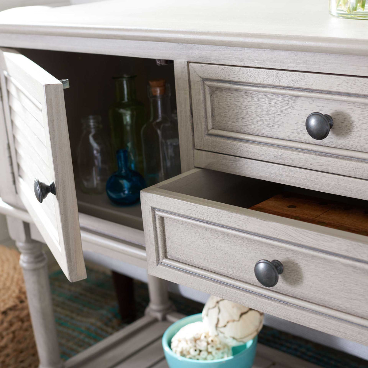 An open drawer and cabinet offer storage for small keepsakes beneath the greige console's tabletop.