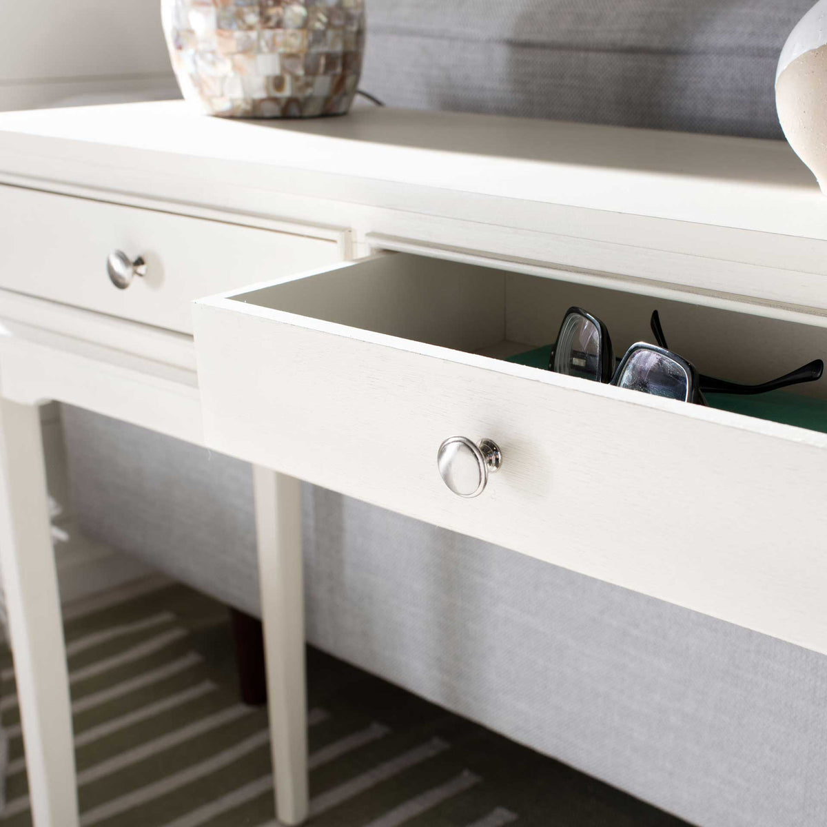 An open distressed white console drawer holds sunglasses and other everyday essentials