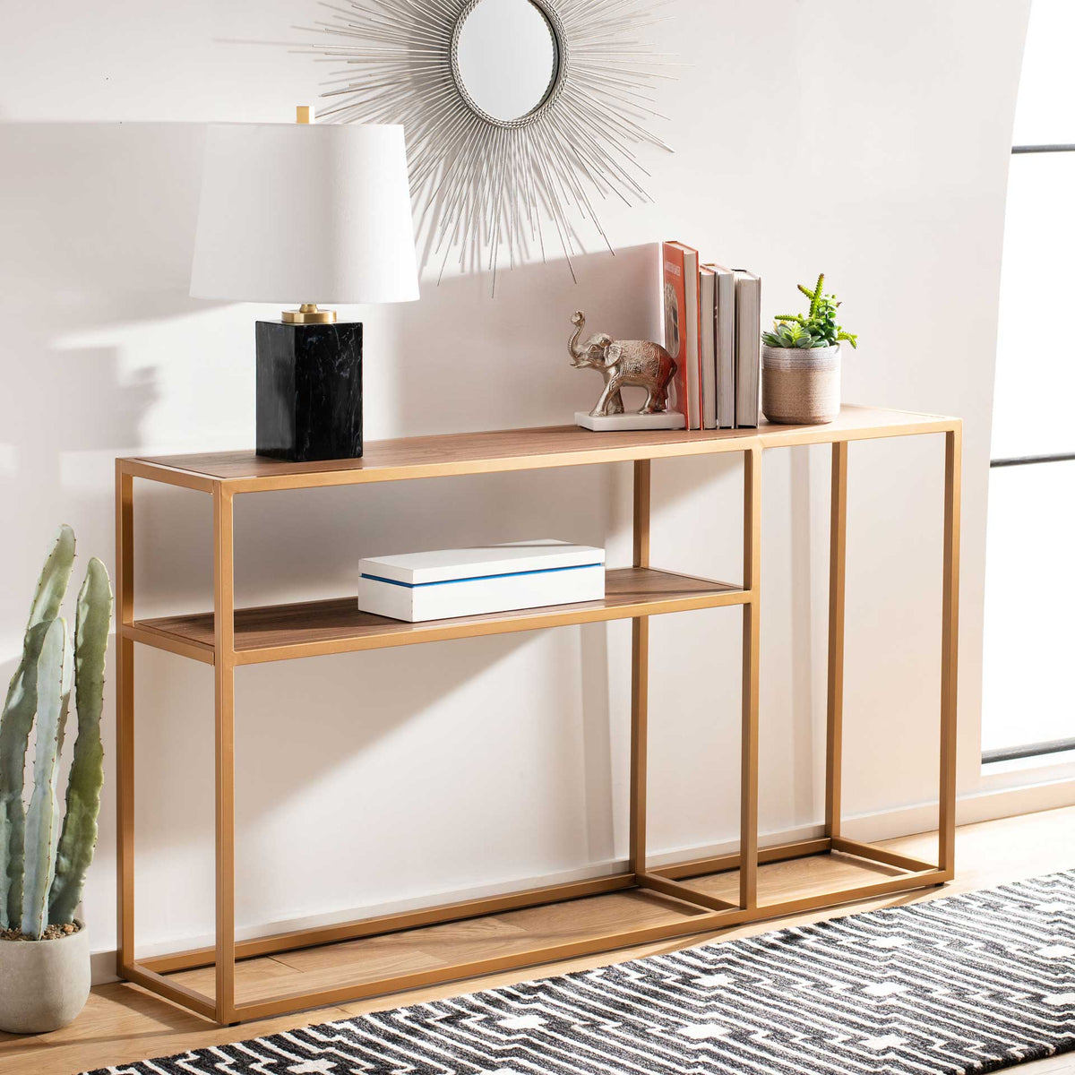 A walnut-finish console with gold framing displays books, a lamp, and small plants.
