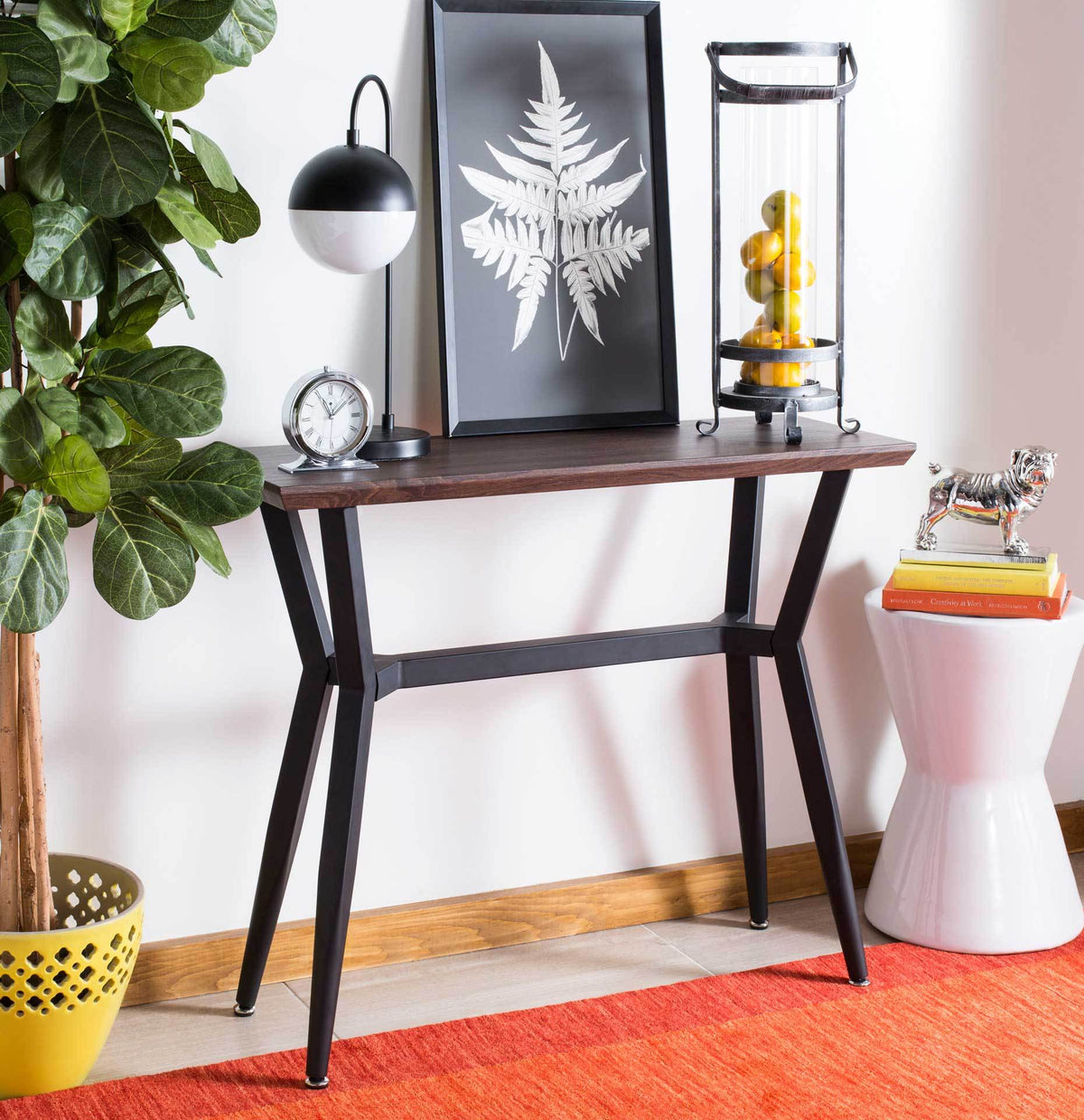 The slim brown tabletop holds lamps and accents above an airy black metal base.