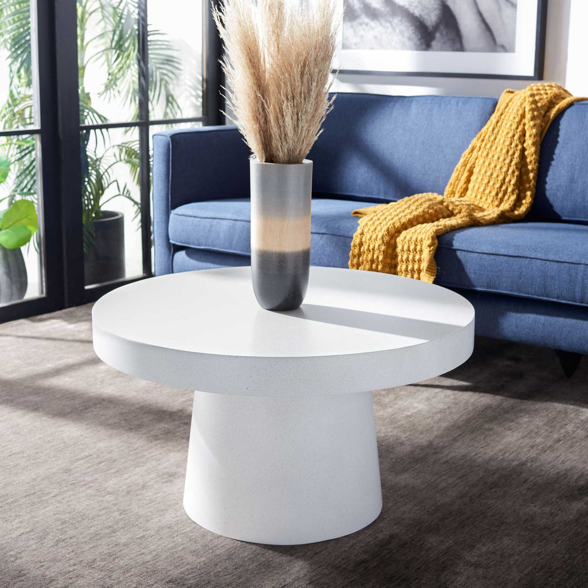 A softly curved pedestal coffee table with a speckled white finish brightens the living room.