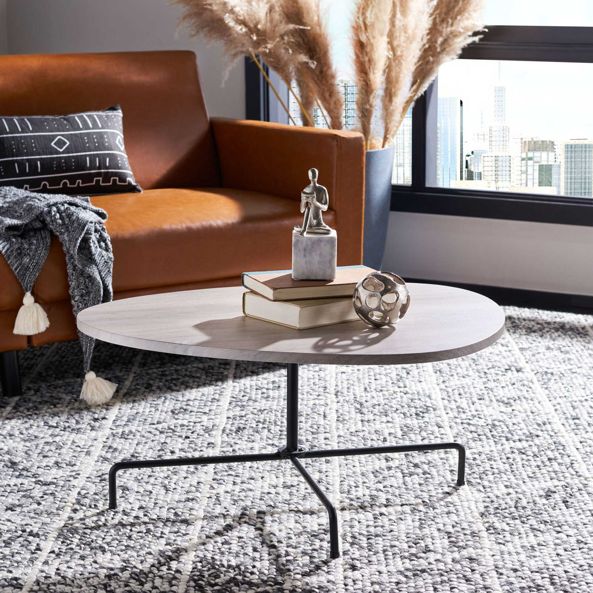 A light gray oak veneer top brings an airy finish to the sleek black tripod coffee table.