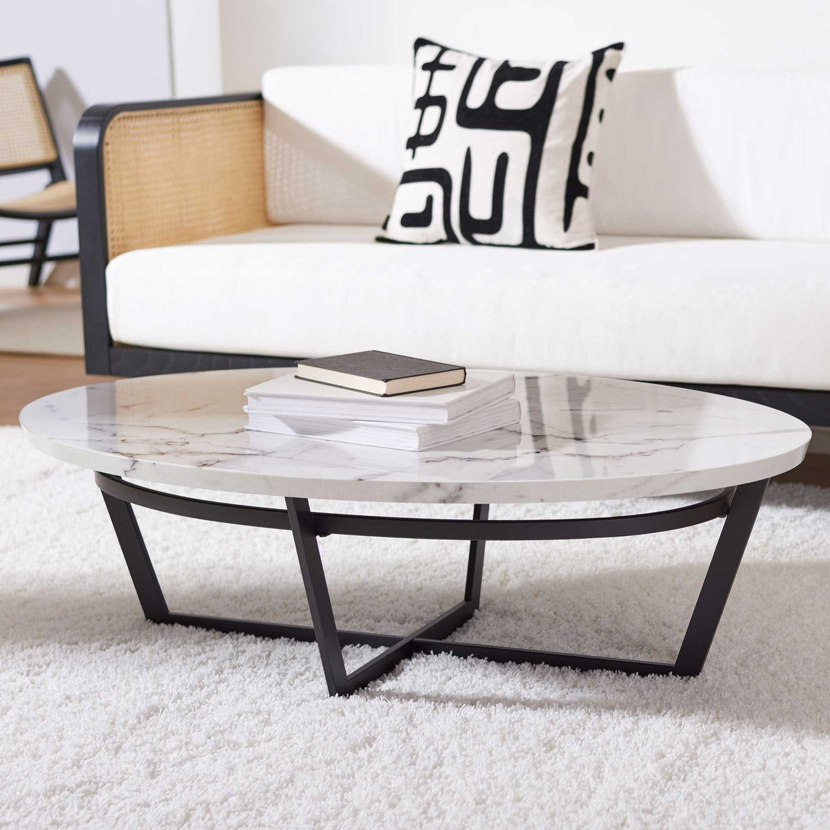 A low oval coffee table brings white marble-look elegance and black metal contrast to a living room.