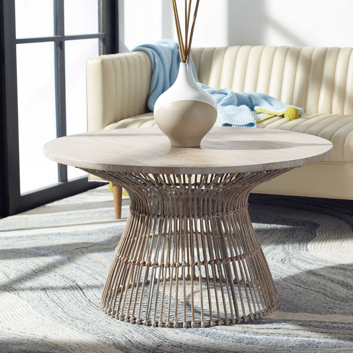 An open rattan pedestal and pale round tabletop bring airy coastal texture to a living room.