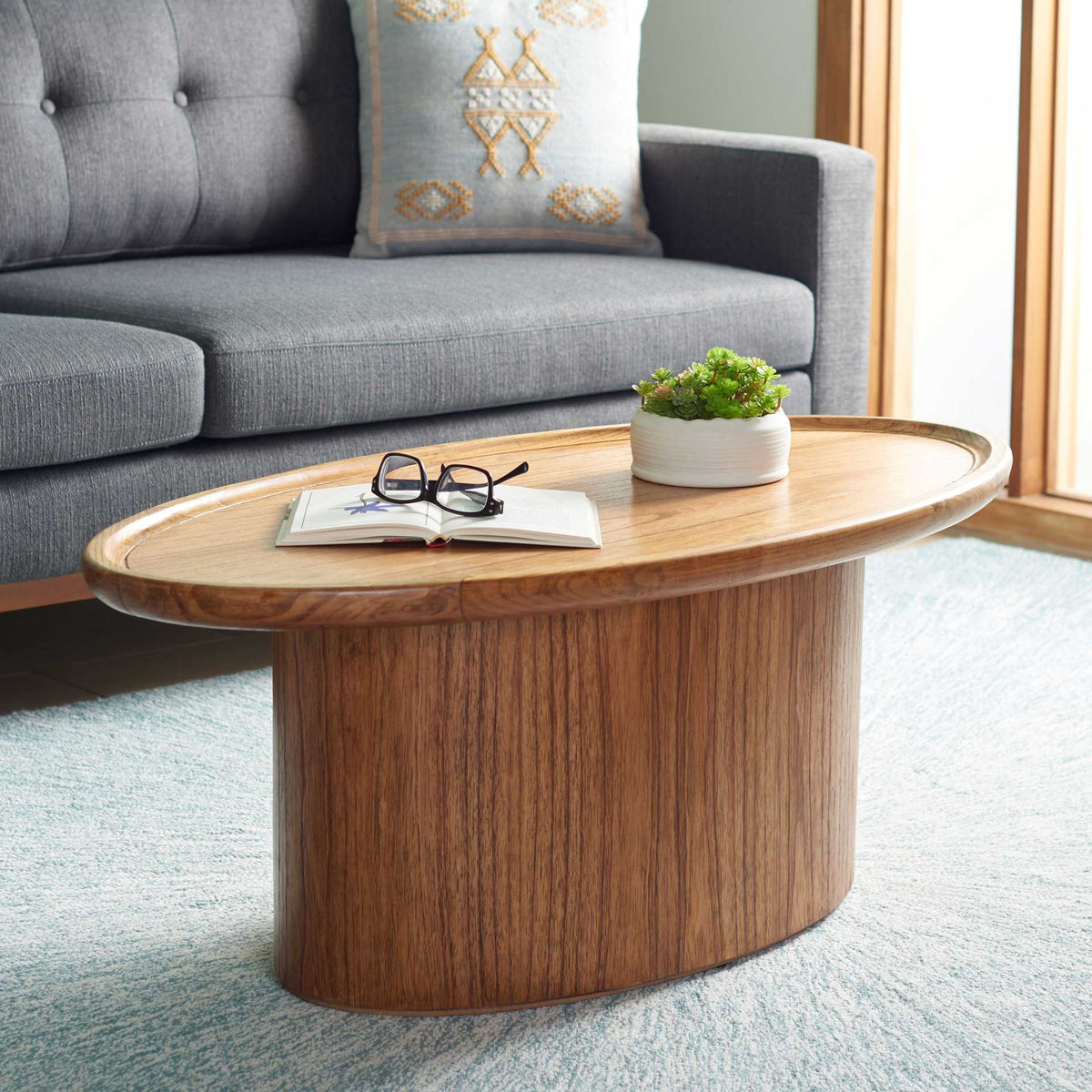 A warm wood oval coffee table anchors the seating area with a spacious top for books and decor.
