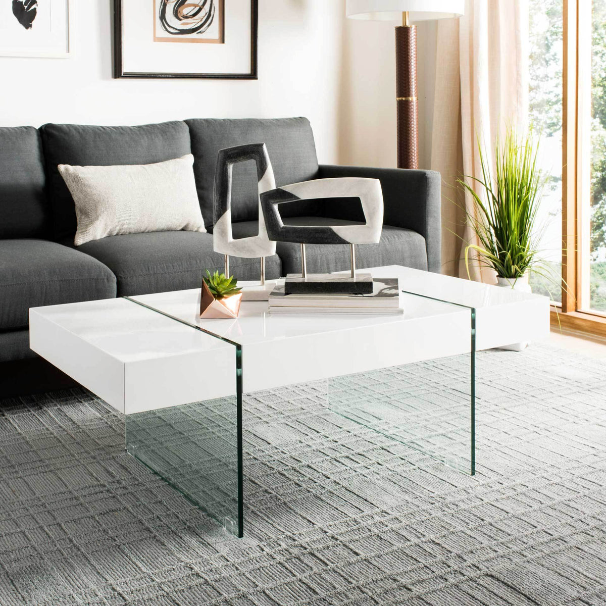 A white tabletop on glass panel legs creates an airy centerpiece beside a charcoal sofa.