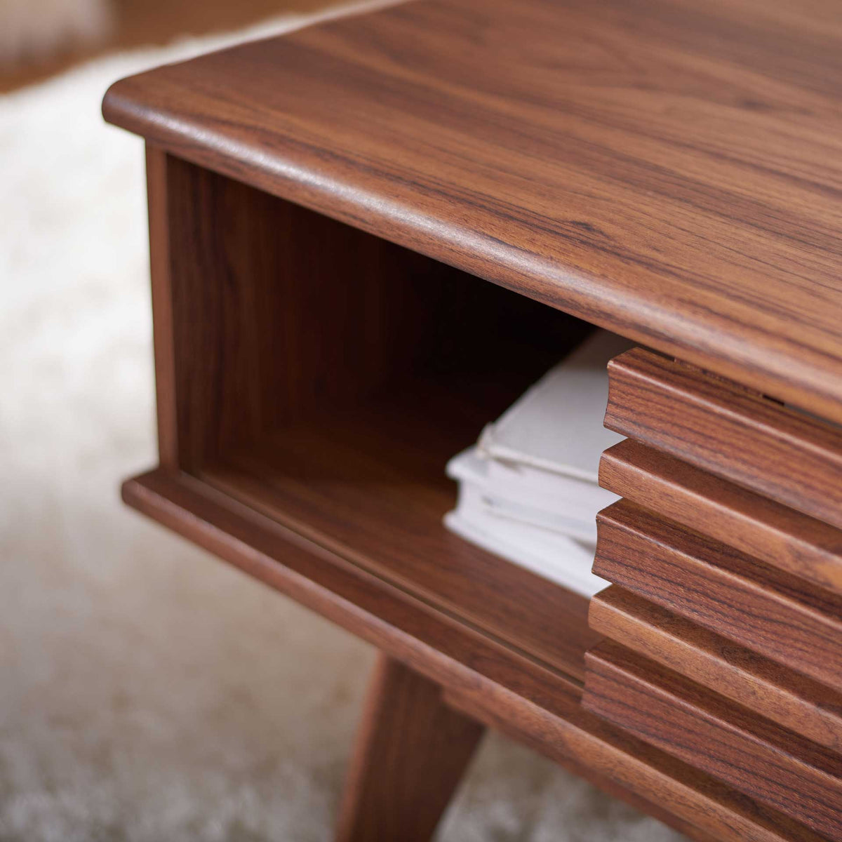 Open storage holds stacked books beneath a walnut-look top beside the slatted door