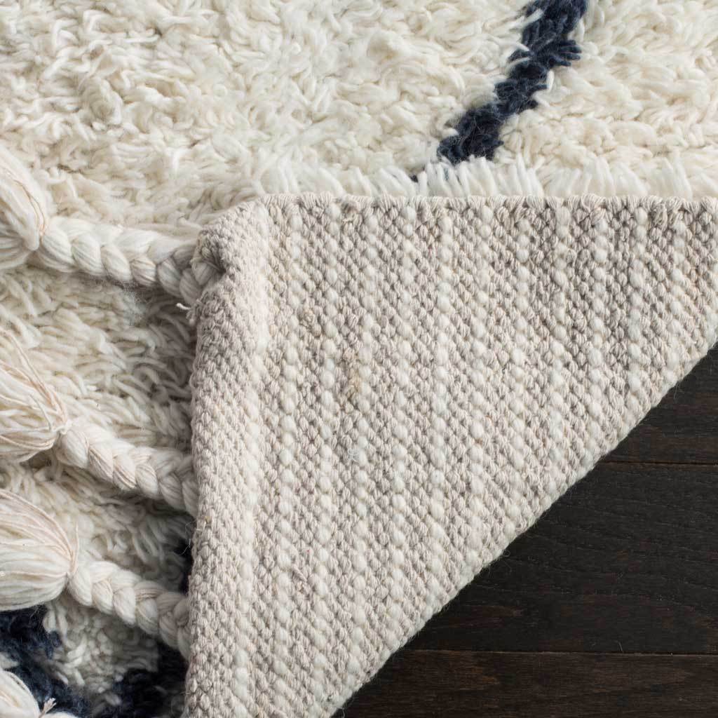 A folded edge reveals tightly woven backing beneath the plush ivory patterned pile.
