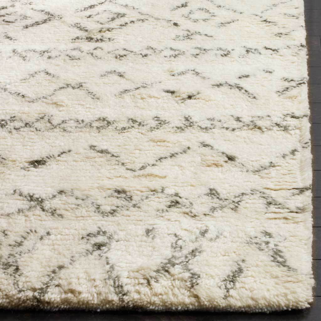 Dense ivory pile and sketchlike gray motifs meet along a thick, finished rug edge