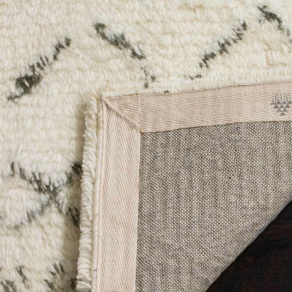 Folded ivory rug corner exposes a woven backing and neatly bound edges