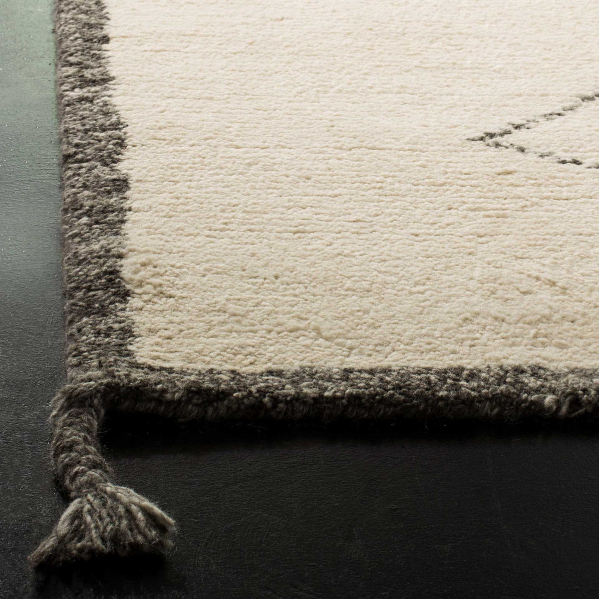 Plush ivory wool pile meets a charcoal border and a thick corner tassel