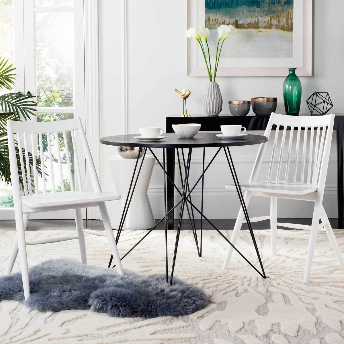 Two white spindle-back chairs brighten a dining nook with a round dark table and light rug.