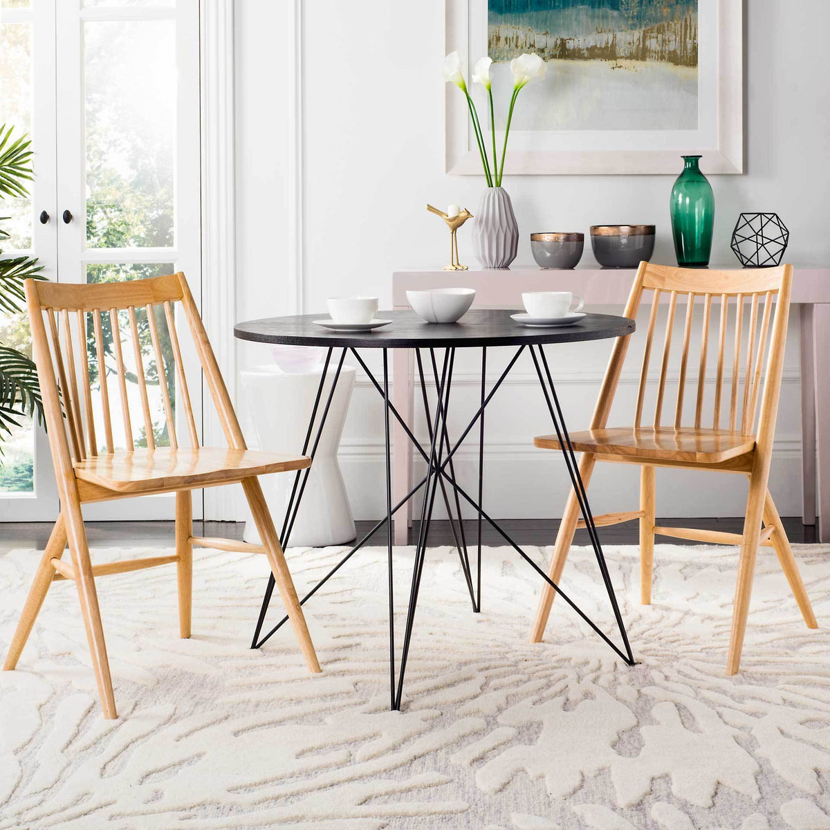 Two natural wood spindle-back chairs add warmth beside a round table in a light-filled room.