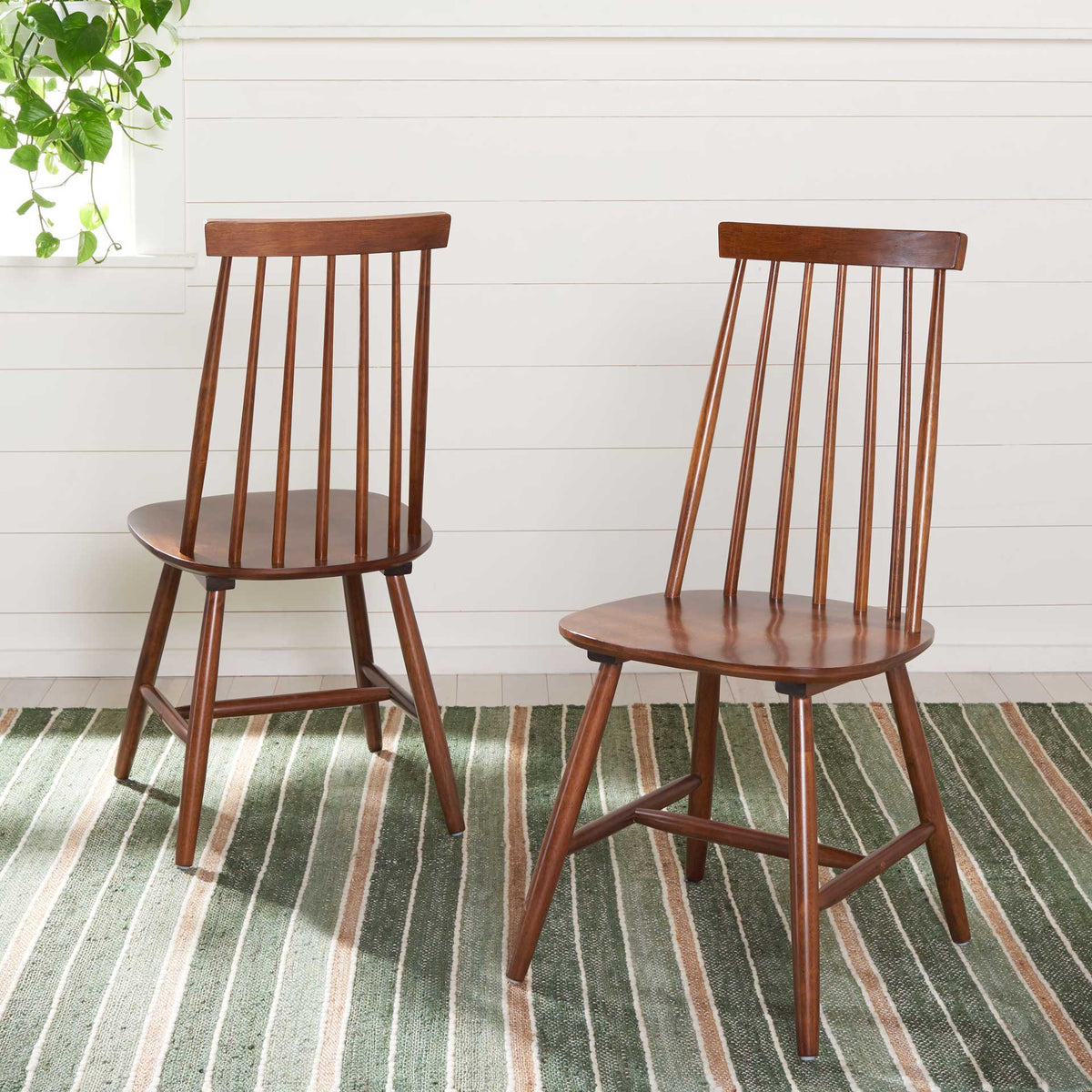 A matching pair of walnut dining chairs pairs airy spindle backs with rounded seats and angled legs.