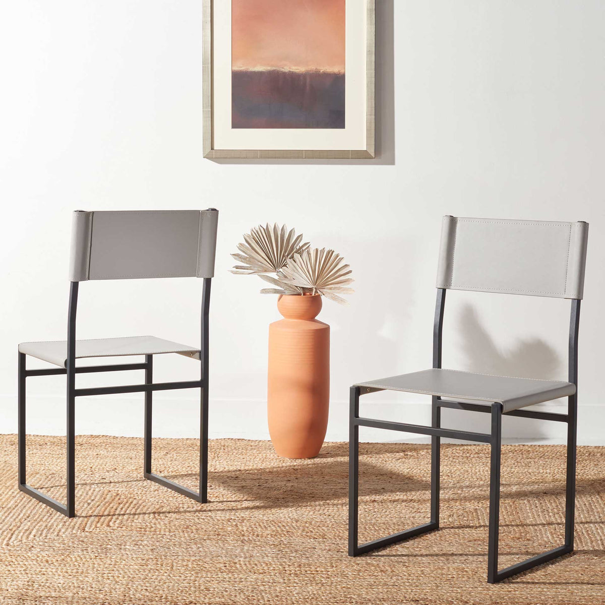 Two light gray leather dining chairs balance soft seats and backs with graphic black metal frames.