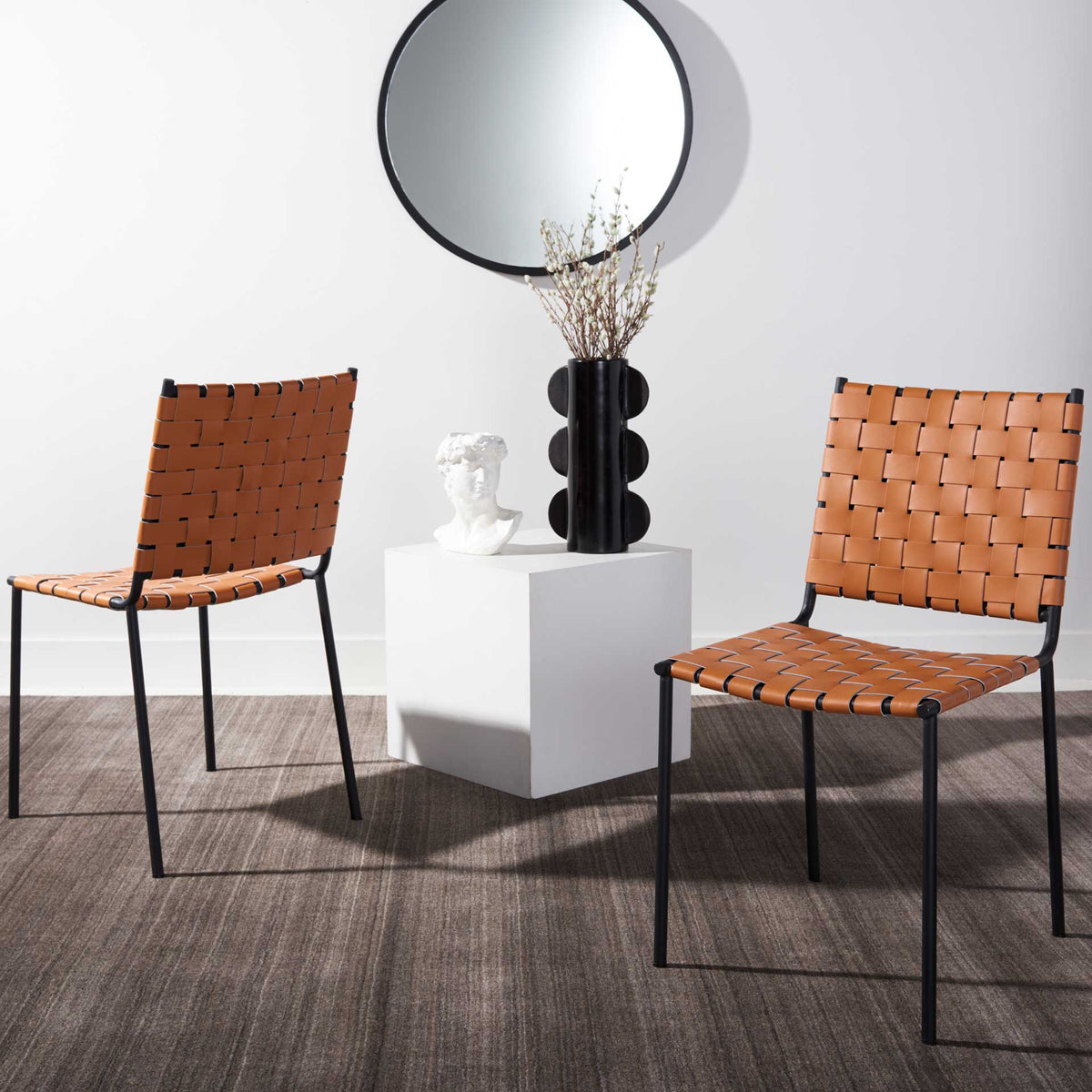 A pair of cognac leather dining chairs brings woven texture and dark metal accents to the room