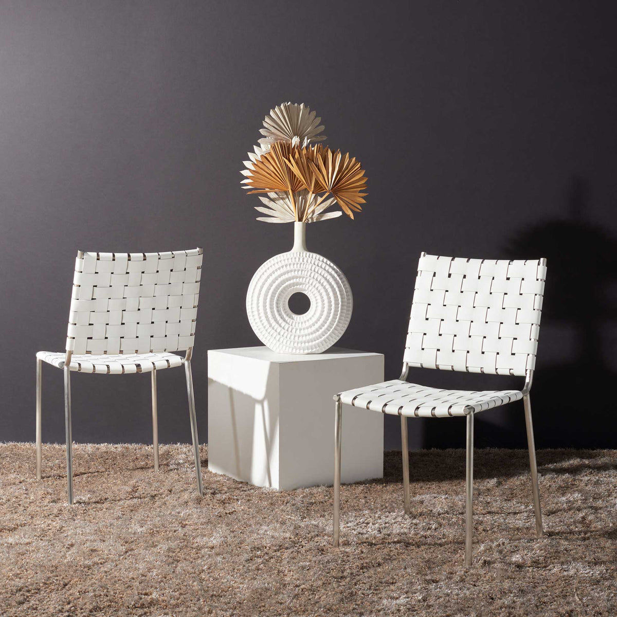 A pair of white leather dining chairs adds bright woven texture against a dark wall