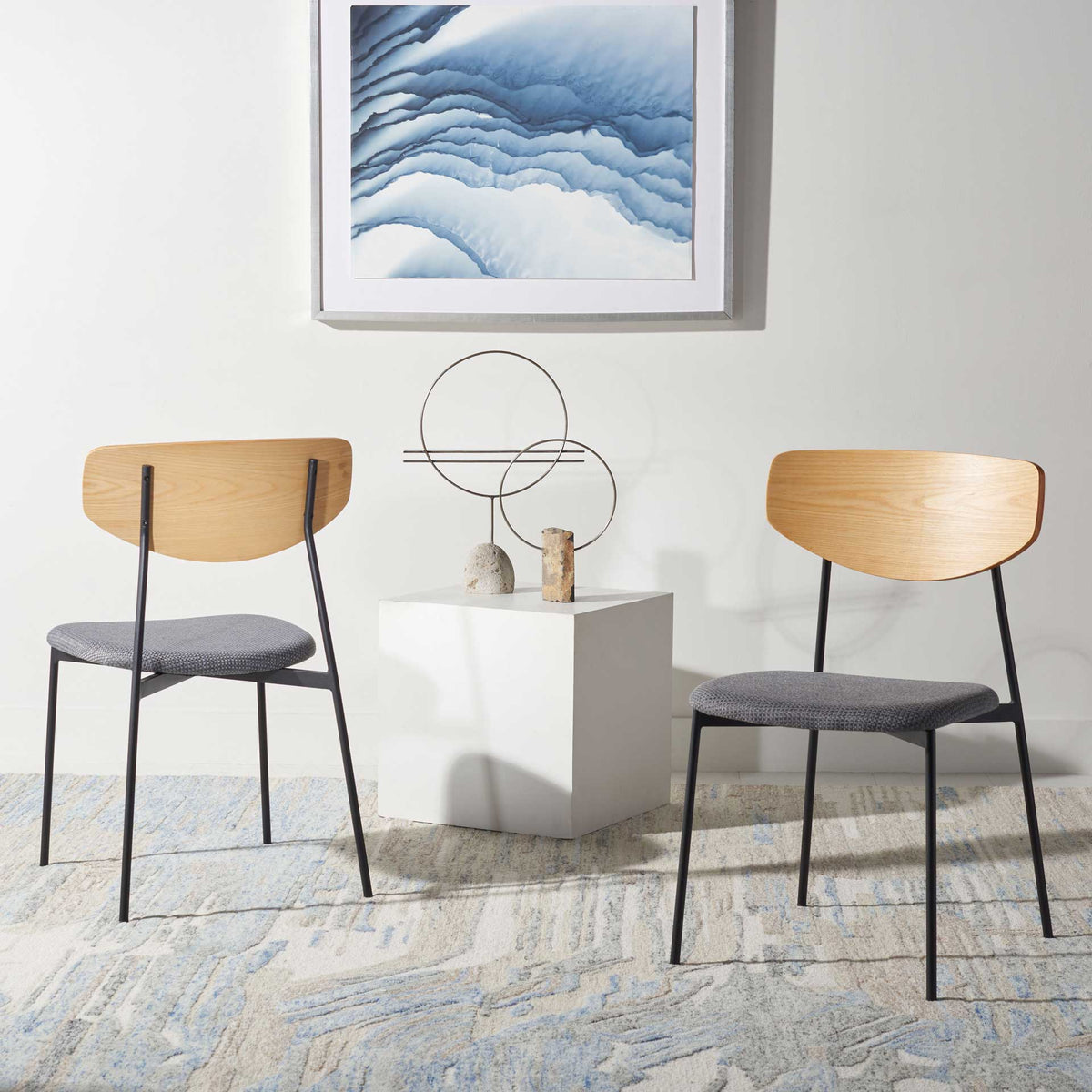 Two oak-finished dining chairs add soft gray seating and airy black frames to a relaxed space.